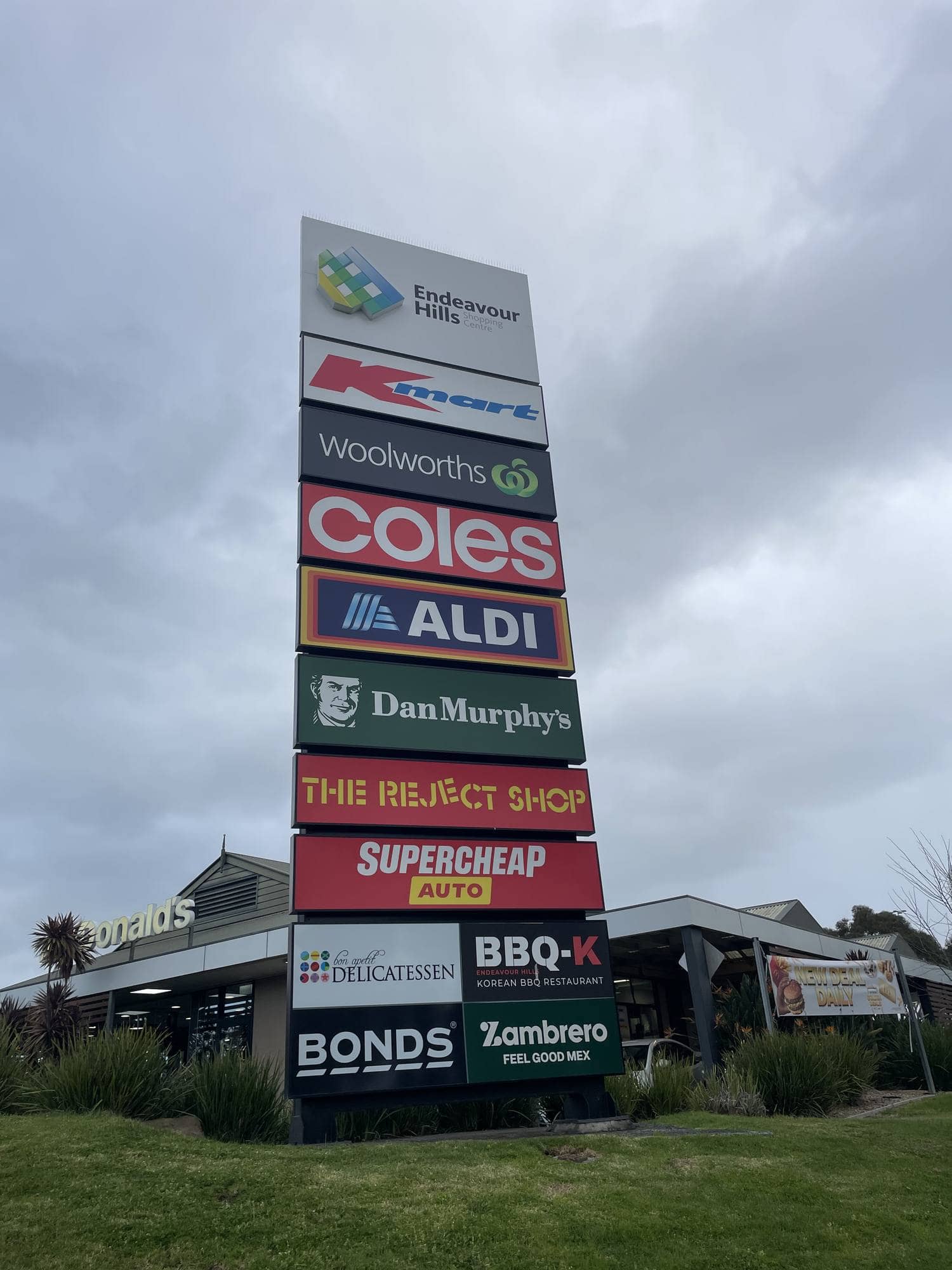 The shopping centre's tall roadside pylon sign, stacked with tenant logos including Kmart, Woolworths, Coles, Aldi, Dan Murphy's, The Reject Shop and Supercheap Auto.