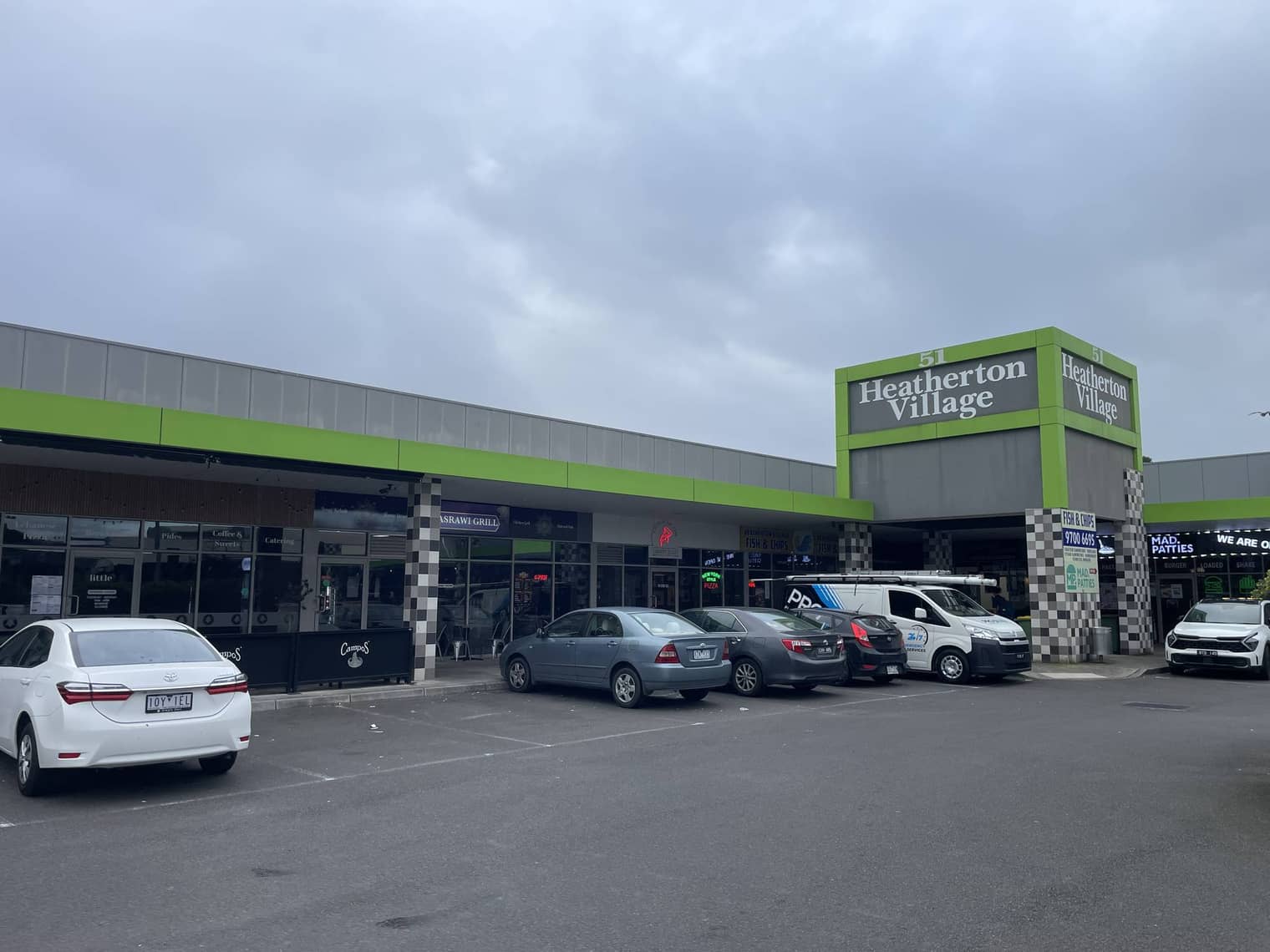 Heatherton Village, a single-storey shopping strip with a green facade and angled parking out front, on Heatherton Road.