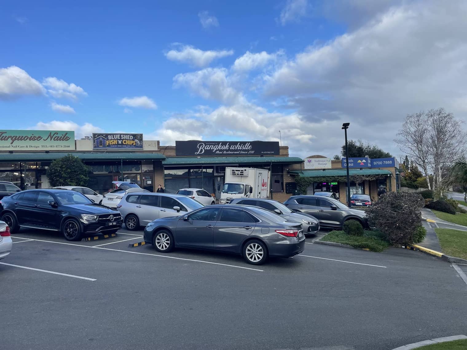 Shops at The Terrace on Raymond McMahon Boulevard — a Thai restaurant, a fish-and-chip shop and a nail salon — seen across the car park.