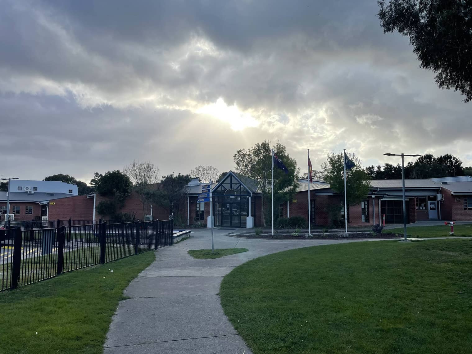 The main entrance of Thomas Mitchell Primary School — a brick building with a pitched portico and flagpoles, with a curved path across the front lawn.